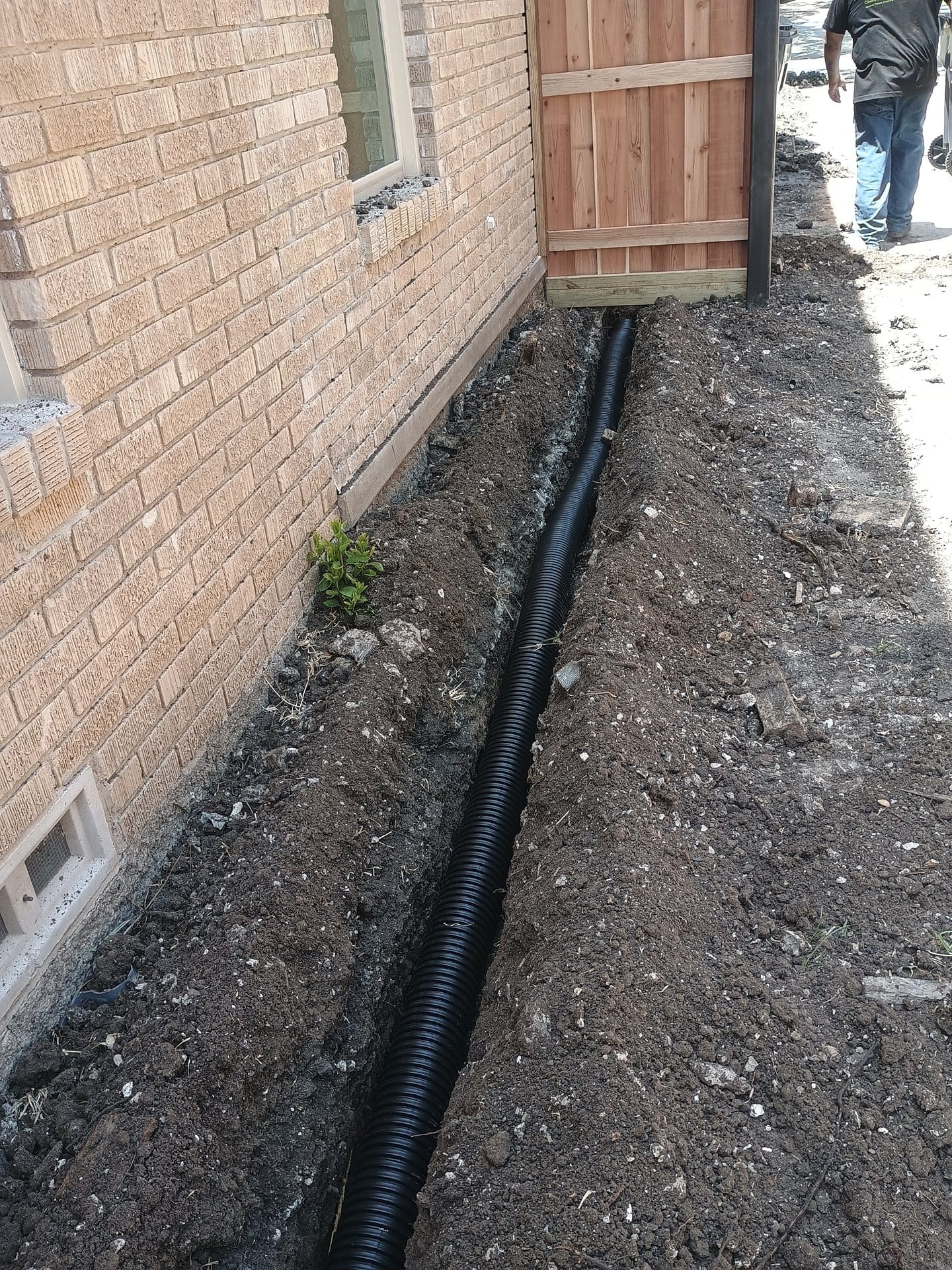 Perforated drainage pipe being installed in gravel-lined trench
