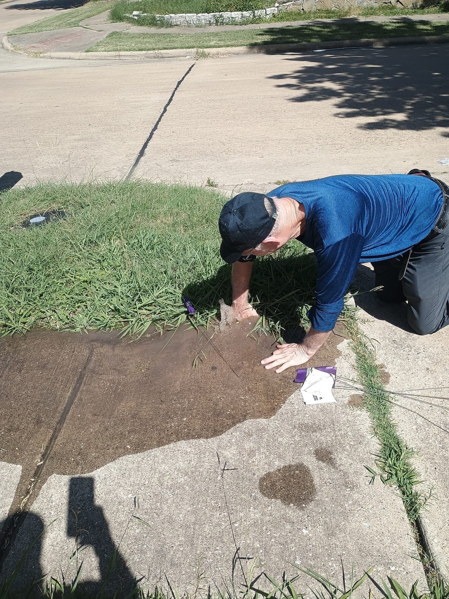 Irrigation technician reaching into excavated hole to diagnose underground pipe leak